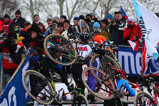 A crowded pack of 'cross racers carry their bikes up a steep grade