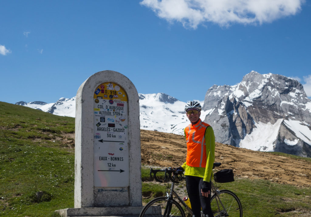 a cyclist clad in safety colors in front of a cairn with rugged snow covered moutains in the backround