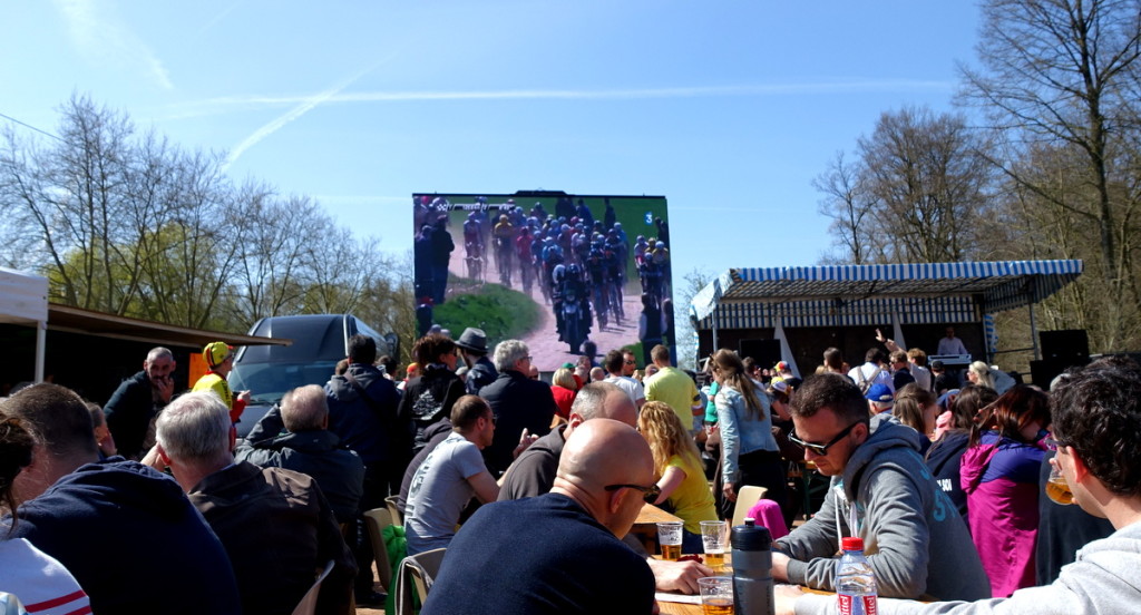 Crowded outdoor dining with racing on a big projection screen and an announcer
