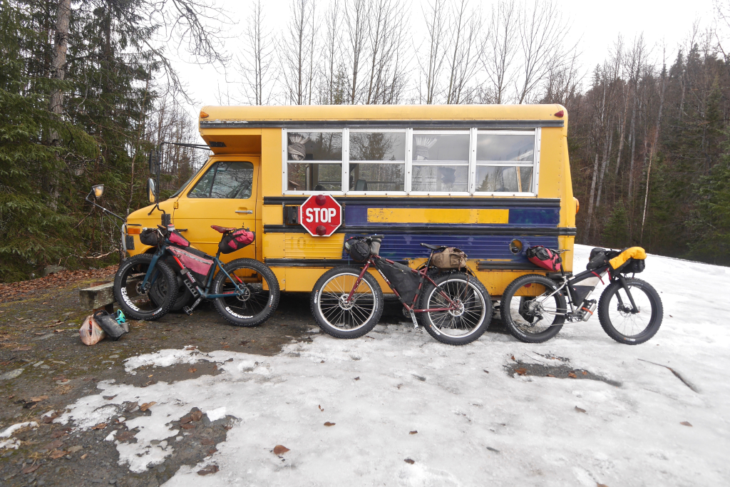 Three bikepacking bikes lean against a bus in winter