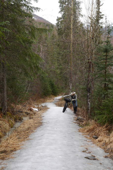 a bikepacker pushes her bike up an ice-capped trail