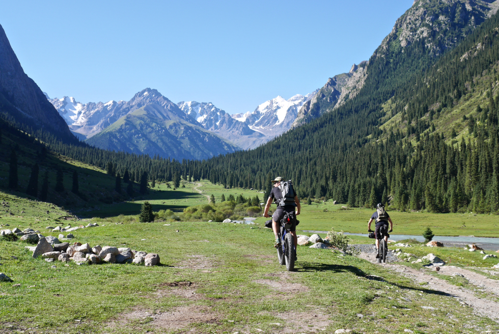Two bikepacking cyclist descent towards a valley stream in Kyrgyzstan