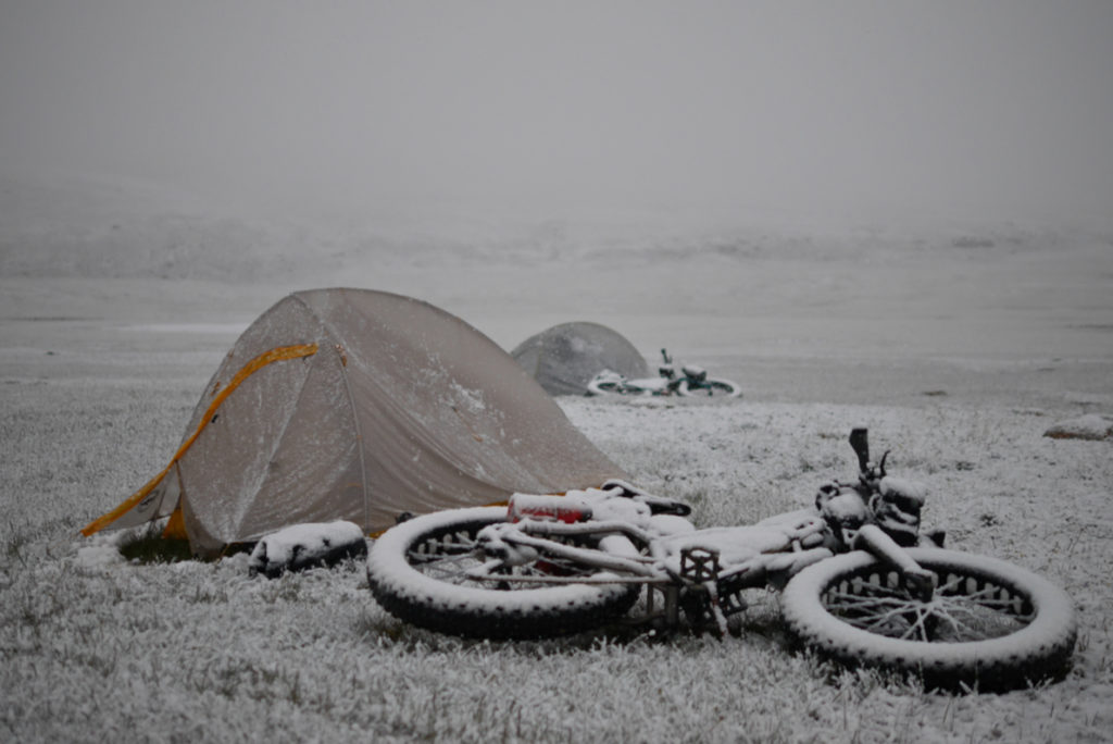 A lonely campsite of two bivy sacks and two prone bicycles covered by a snowstorm