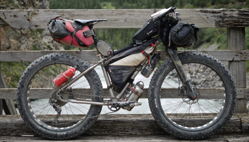 Joe's Seven Treeline SL, loaded to the gills for a bikepacking adventure, leans against a wooden bridge wall