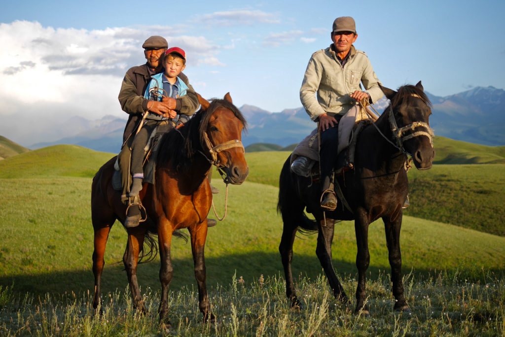 Two rugged horsemen and a child in the rolling foothills of Kyrgyzstan