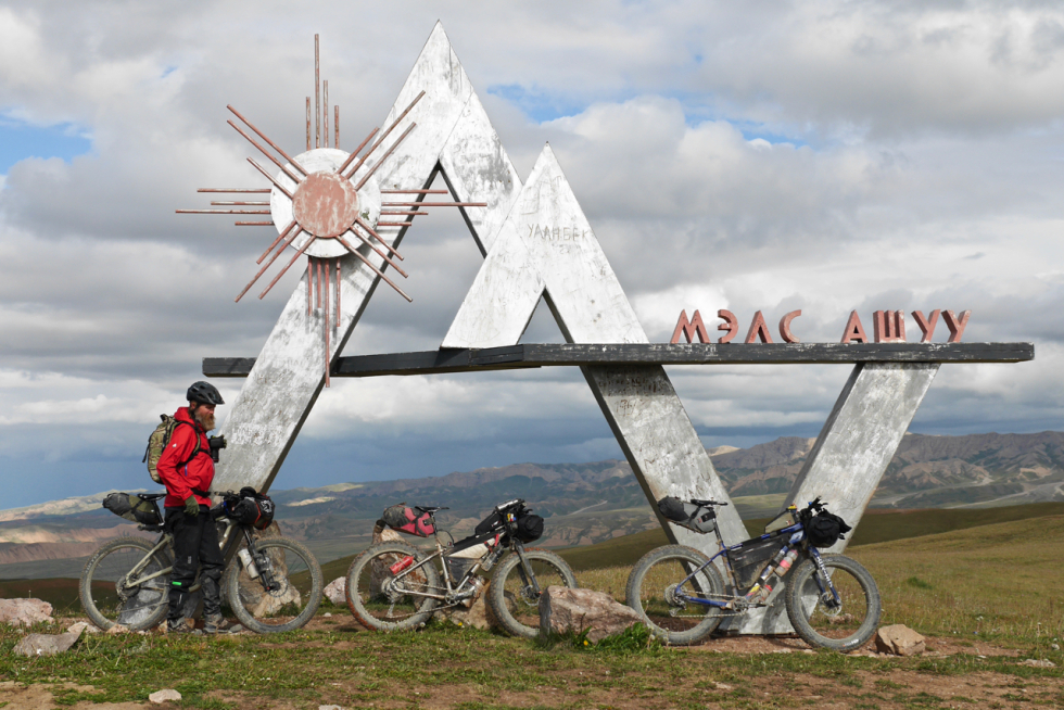 Three bikepacking bikes rest agains a Kyrgyzstan sculptural sign