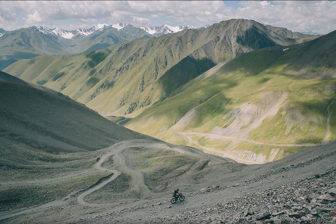 a distant rider navigates his way down a rocky road through a dramatic mountain range which can be seen for hundreds of miles