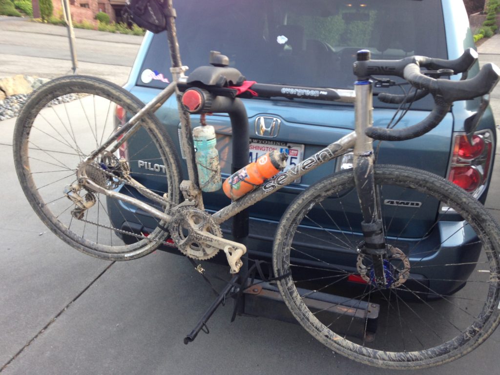 a muddy Seven Evergreen PRO hangs on the back rack of a car