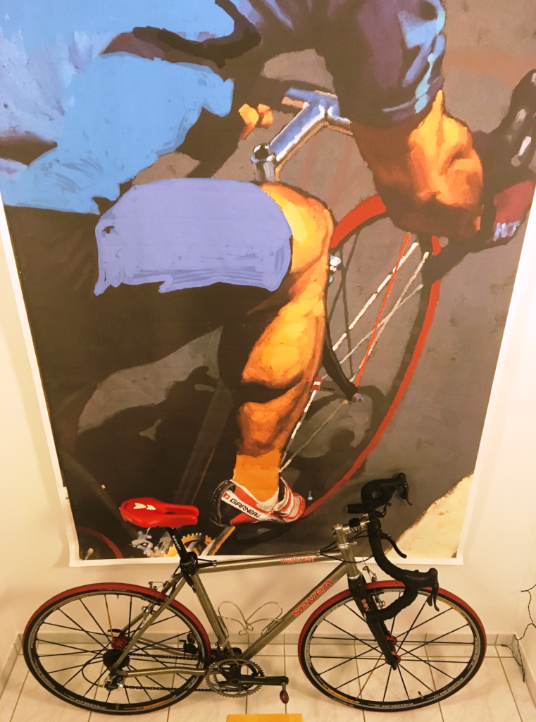 A huge painting of a cyclist hangs behind a real-life version of the bike