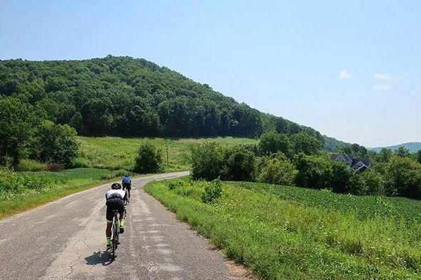 two riders ride away on a county road on a sunny day