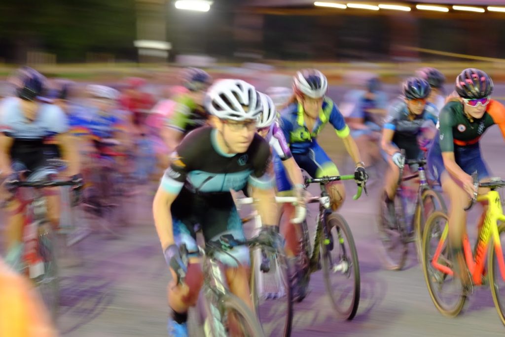 Kelly Cataly leads a pack of colorfully clad cyclocross racers at night