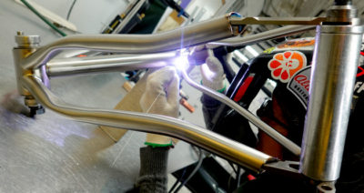 a beautiful titanium bicycle frame is being welded on a shiny aluminum bench