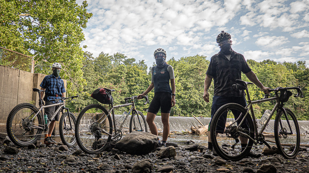 Three socailly distanced and masked riders in the shade and in front of a waterfall.