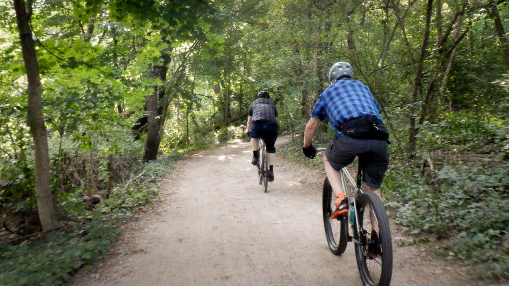 Two bicycle riderss flying on the smooth forest gravel trail in the summertime.