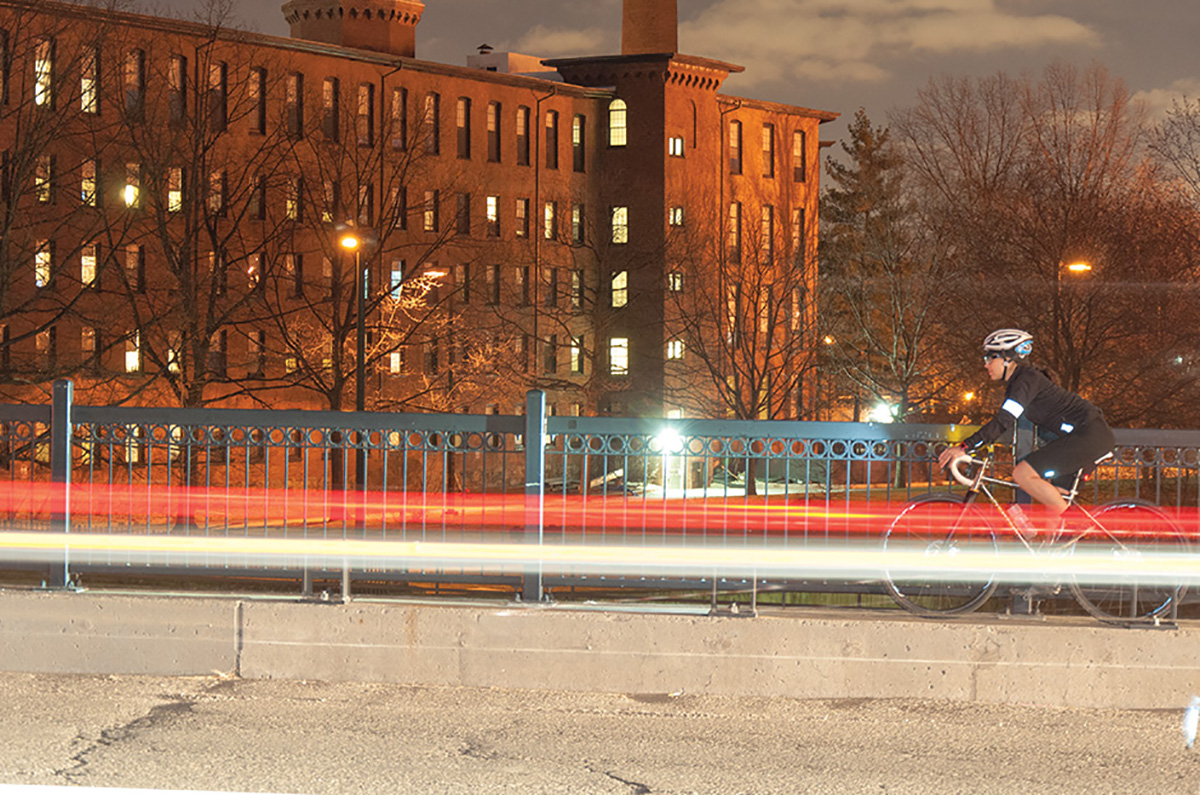 night cyclist crossing a bridge near a mill