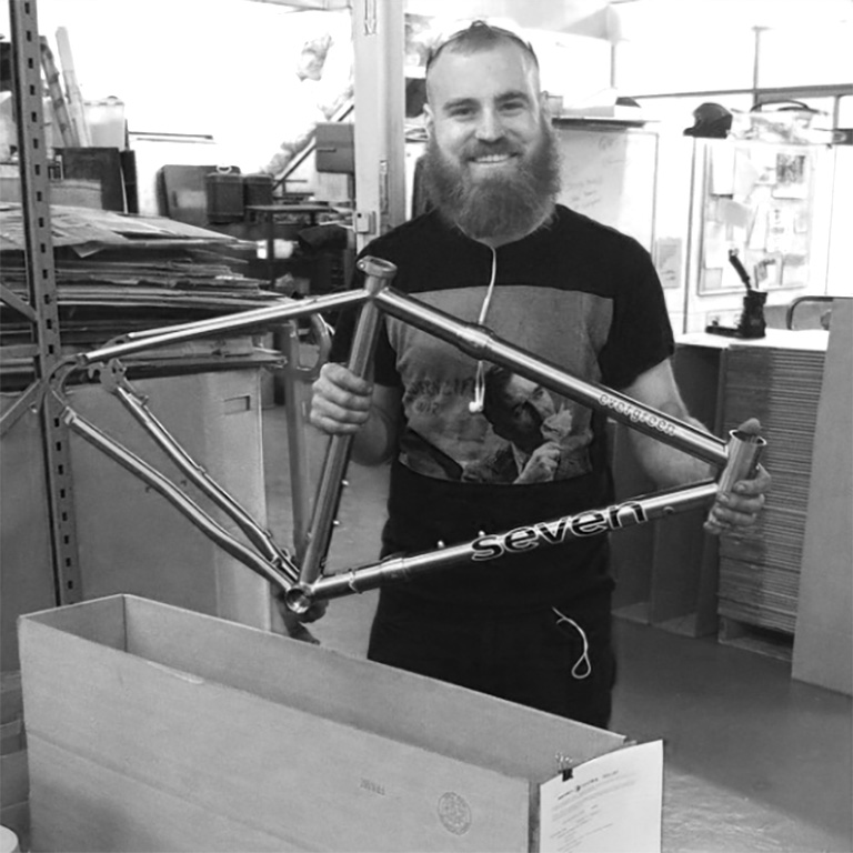 a smiling Seven finisher puts a finished bicycle frame into a shipping box