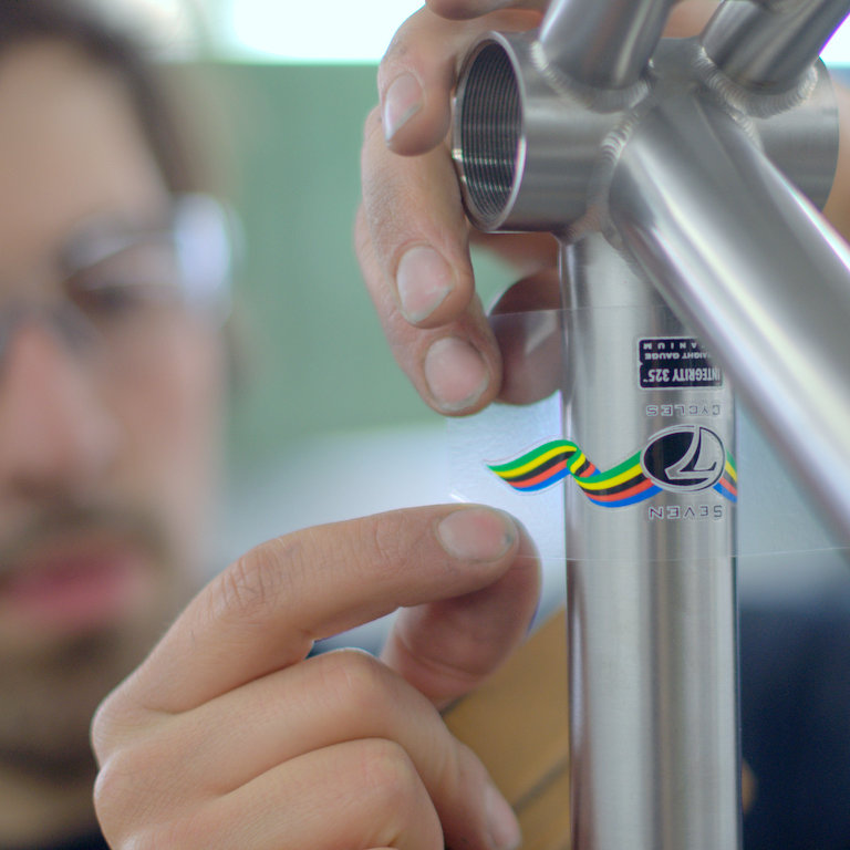a finisher carefully applies a decal to a titanium bike